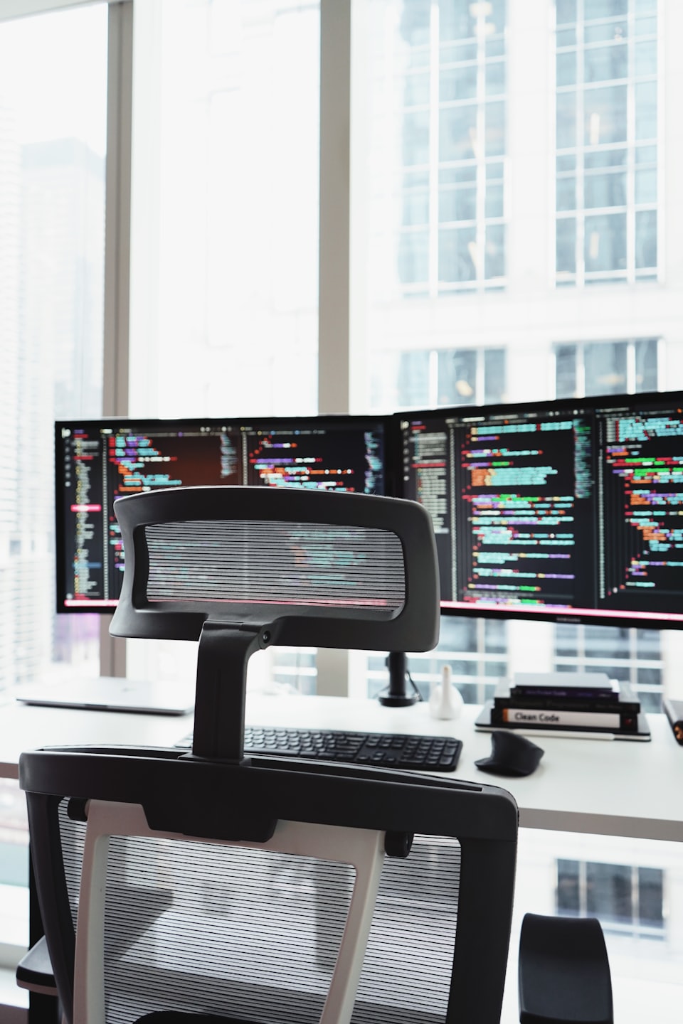 白い机の上にコードが表示された2台のコンピューターモニター。